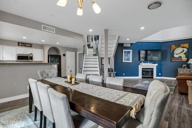 dining room featuring visible vents, stairway, wood finished floors, a tile fireplace, and baseboards