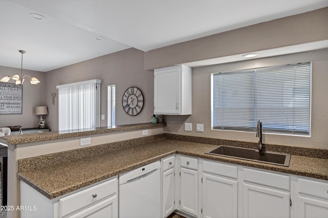 kitchen with dark countertops, white dishwasher, a sink, and a peninsula