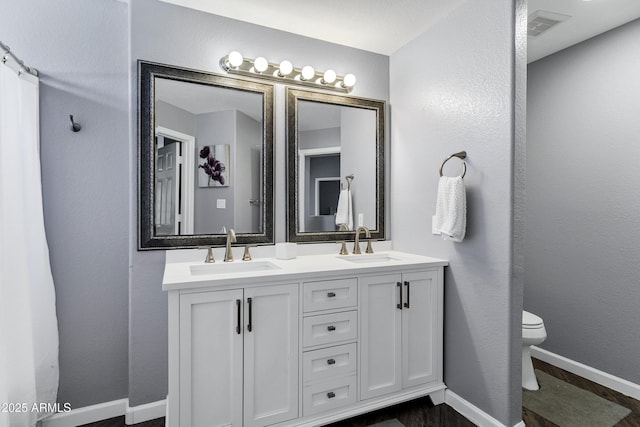 bathroom featuring toilet, a sink, visible vents, and baseboards