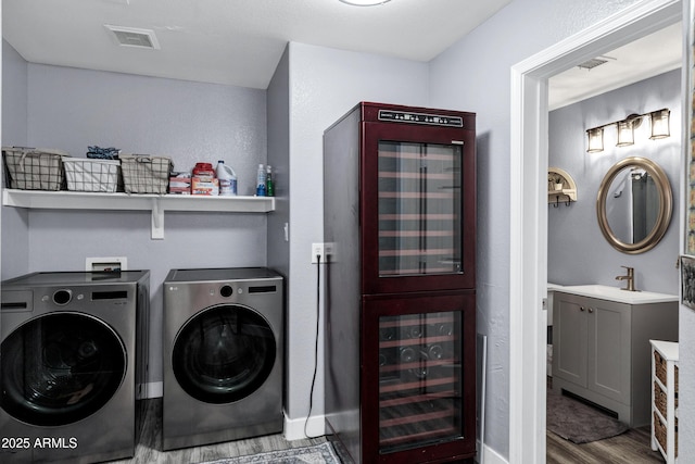 washroom featuring wine cooler, laundry area, wood finished floors, a sink, and washing machine and clothes dryer