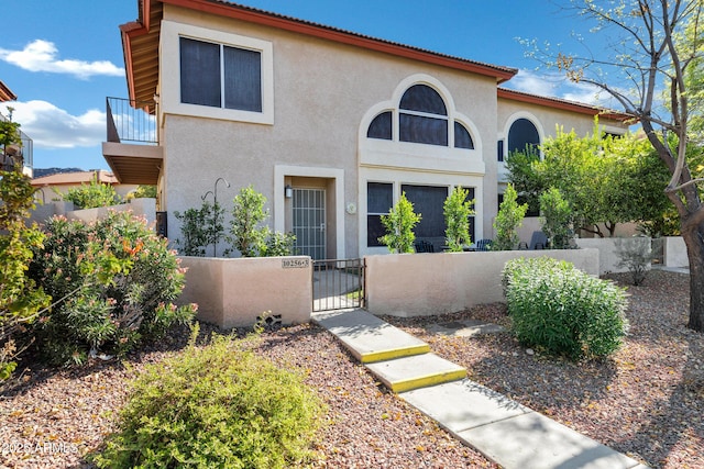 view of front facade with a fenced front yard, a balcony, a gate, and stucco siding