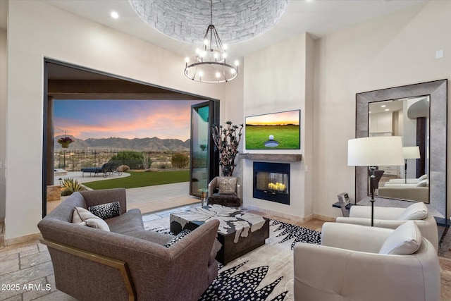 living area featuring baseboards, a glass covered fireplace, a high ceiling, an inviting chandelier, and stone tile floors