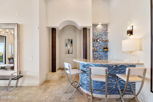 bar with baseboards, a towering ceiling, indoor wet bar, and stone tile flooring