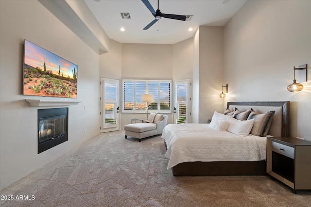 carpeted bedroom featuring recessed lighting, access to outside, a towering ceiling, visible vents, and a glass covered fireplace