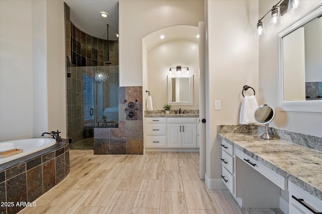 bathroom featuring a bath, a sink, a stall shower, and two vanities