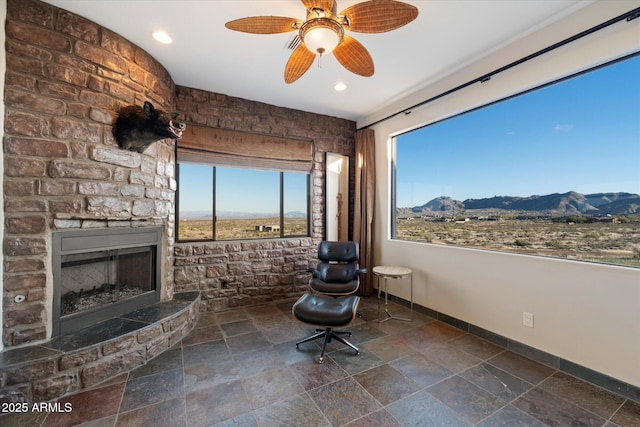 unfurnished room featuring baseboards, ceiling fan, stone tile flooring, a stone fireplace, and a mountain view