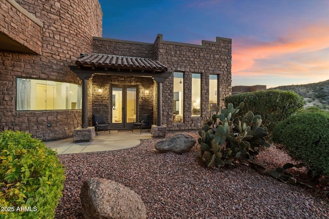 view of exterior entry with stone siding, french doors, and a patio