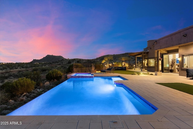 pool at dusk with a mountain view, a pool with connected hot tub, and a patio area