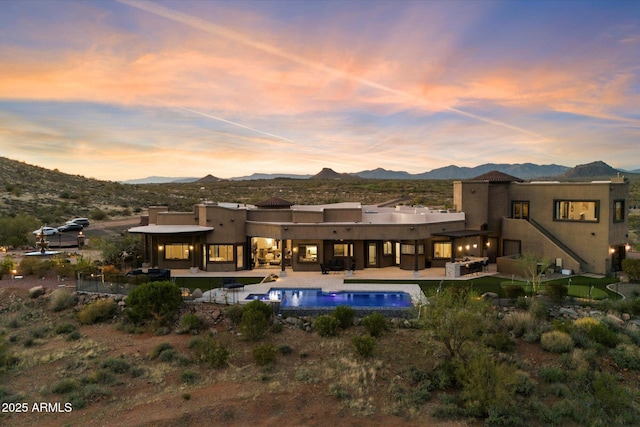 rear view of property featuring stucco siding, an outdoor pool, a patio area, and a mountain view