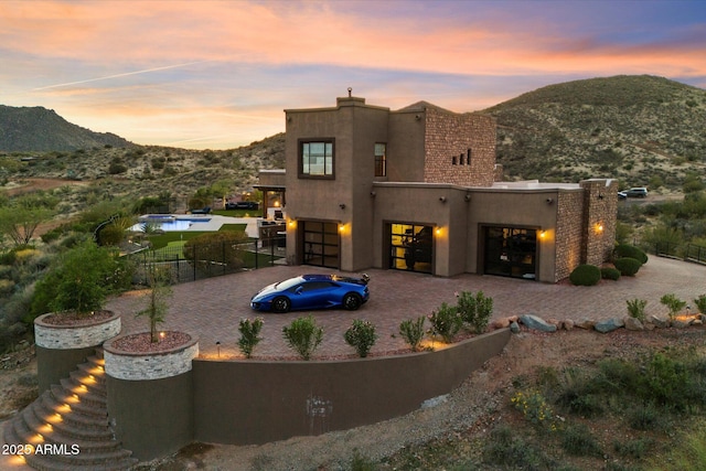 back of house featuring stucco siding, fence, driveway, a mountain view, and a chimney