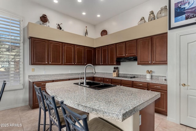 kitchen with light tile patterned floors, a sink, light countertops, a kitchen breakfast bar, and under cabinet range hood