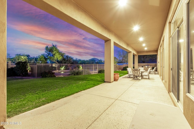 patio terrace at dusk featuring outdoor dining space, a yard, and a fenced backyard