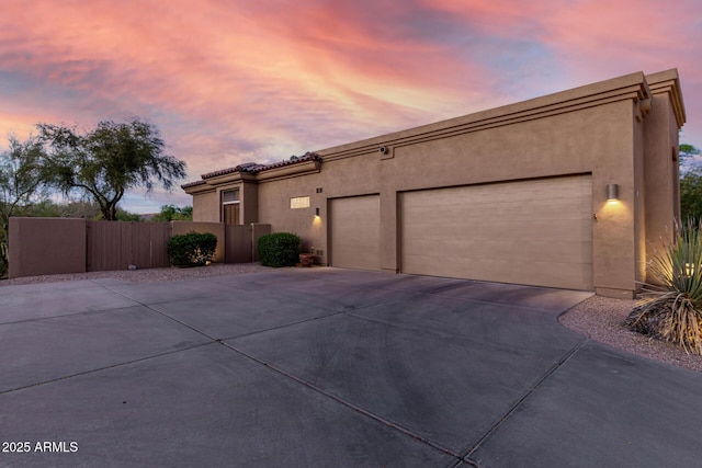 view of front of house featuring concrete driveway, stucco siding, a tile roof, a garage, and fence