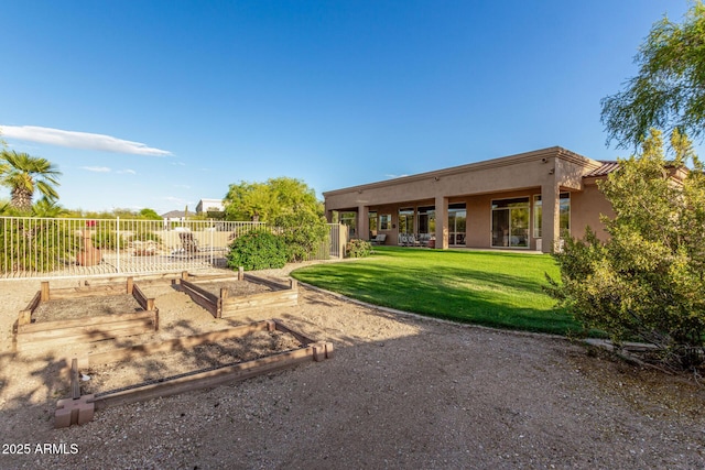 rear view of house with a garden, a yard, stucco siding, and fence