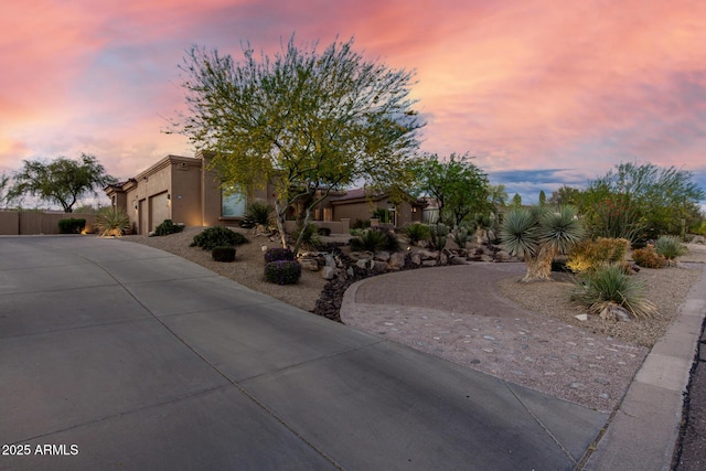 view of front of property featuring curved driveway, fence, a garage, and stucco siding