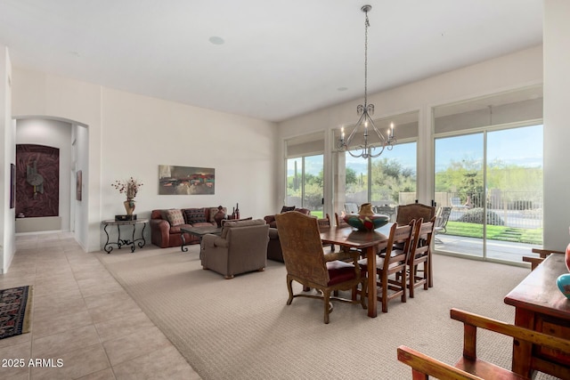 dining space with arched walkways, an inviting chandelier, carpet flooring, and tile patterned flooring