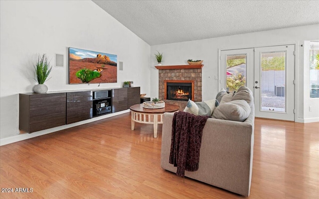 living room with french doors, vaulted ceiling, a textured ceiling, and light wood-type flooring