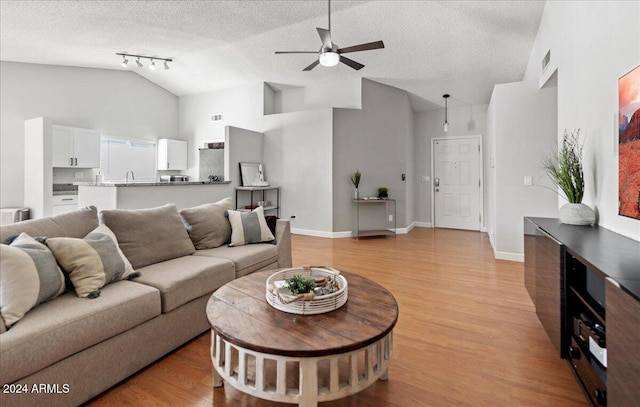 living room with rail lighting, light hardwood / wood-style floors, high vaulted ceiling, and a textured ceiling