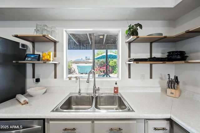 kitchen featuring light countertops, a sink, stainless steel dishwasher, and open shelves