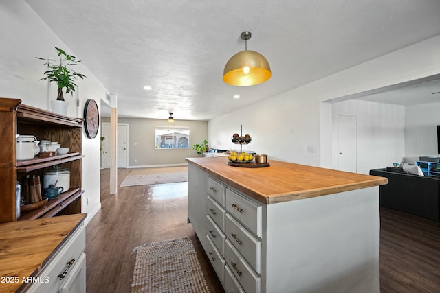 kitchen with butcher block counters, open floor plan, dark wood-style flooring, a center island, and gray cabinetry