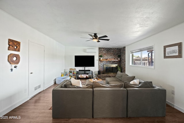 living area featuring visible vents, a ceiling fan, wood finished floors, a brick fireplace, and a wall mounted AC