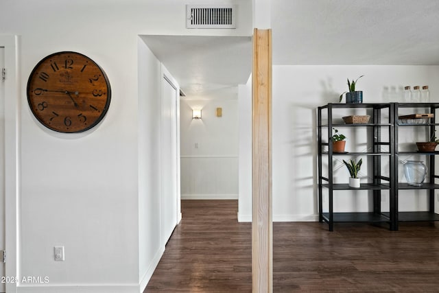 hallway with baseboards, visible vents, and wood finished floors