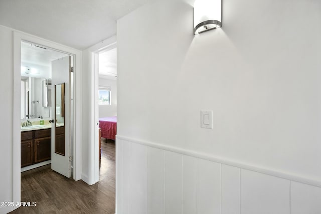 hall featuring a wainscoted wall, a sink, and dark wood finished floors