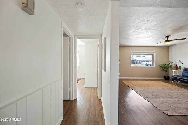 hallway featuring visible vents, a textured ceiling, baseboards, and wood finished floors