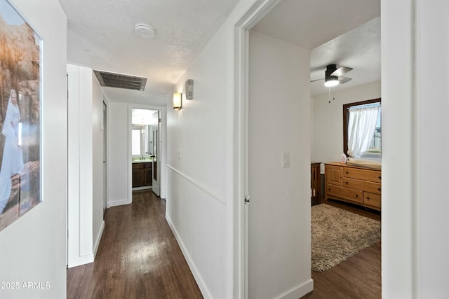 corridor featuring dark wood-style flooring, visible vents, and baseboards