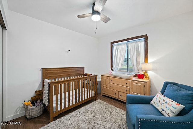 bedroom with a nursery area, wood finished floors, a ceiling fan, and baseboards