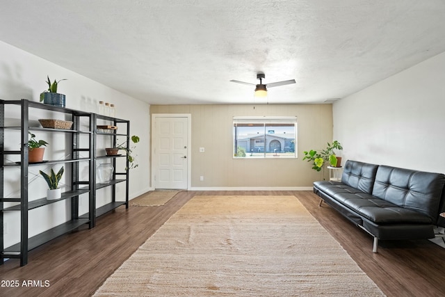 living room featuring a ceiling fan, a textured ceiling, baseboards, and wood finished floors