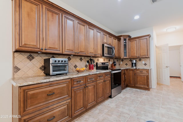 kitchen featuring a toaster, stainless steel appliances, backsplash, brown cabinetry, and glass insert cabinets