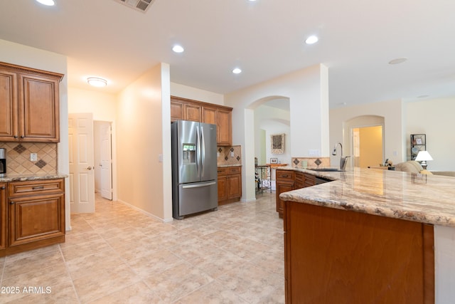 kitchen with light stone countertops, brown cabinets, a sink, and stainless steel fridge with ice dispenser