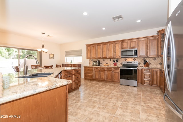 kitchen with a sink, visible vents, appliances with stainless steel finishes, backsplash, and brown cabinetry