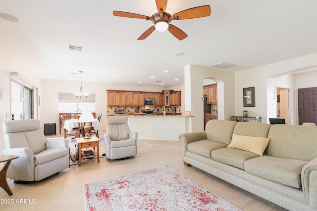 living area featuring light wood-style floors, recessed lighting, visible vents, and ceiling fan with notable chandelier