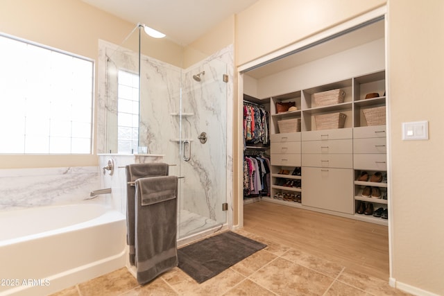 bathroom featuring a walk in closet, a garden tub, and a marble finish shower