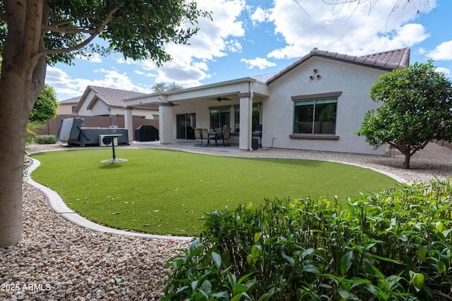 rear view of house with ceiling fan, fence, a lawn, stucco siding, and a patio area