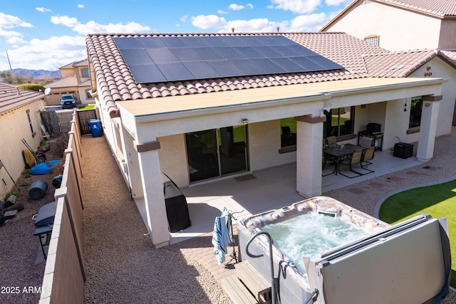 rear view of property with an outdoor hot tub, solar panels, a fenced backyard, a tiled roof, and stucco siding