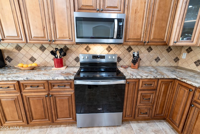 kitchen with light stone countertops, brown cabinetry, stainless steel appliances, and decorative backsplash