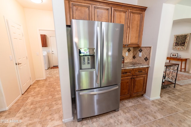 kitchen featuring washer / dryer, stainless steel fridge, decorative backsplash, light stone counters, and brown cabinets