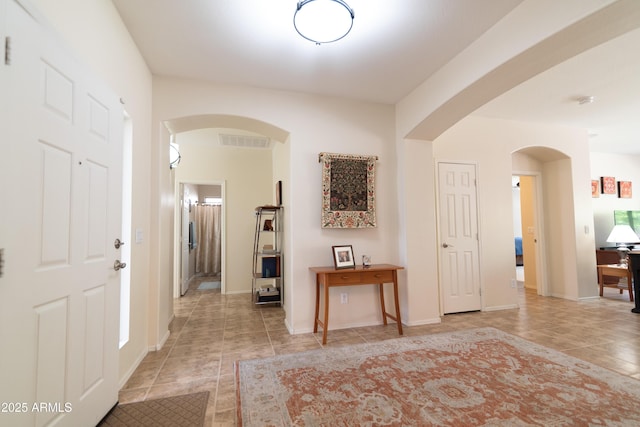 entrance foyer featuring arched walkways, light tile patterned flooring, visible vents, and baseboards