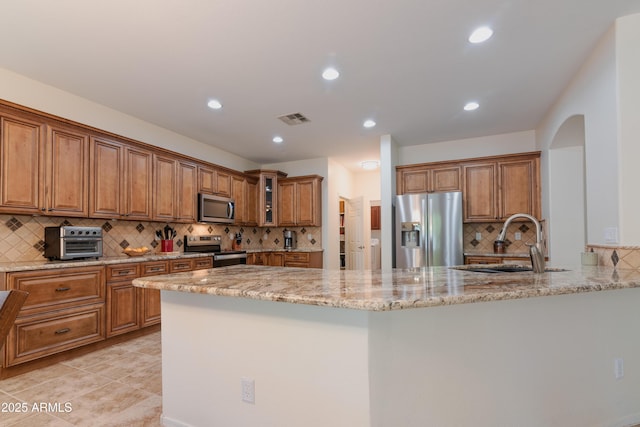 kitchen featuring a sink, visible vents, appliances with stainless steel finishes, brown cabinets, and light stone countertops