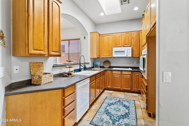 kitchen featuring light tile patterned flooring, white appliances, a skylight, and sink