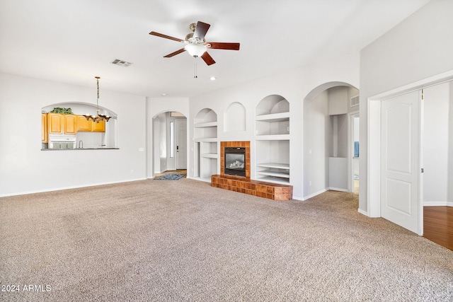 unfurnished living room featuring carpet flooring, built in shelves, a fireplace, and ceiling fan with notable chandelier