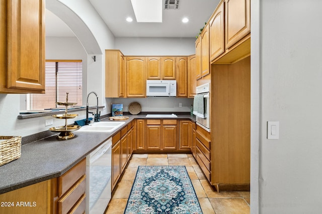 kitchen featuring light tile patterned flooring, white appliances, a skylight, and sink