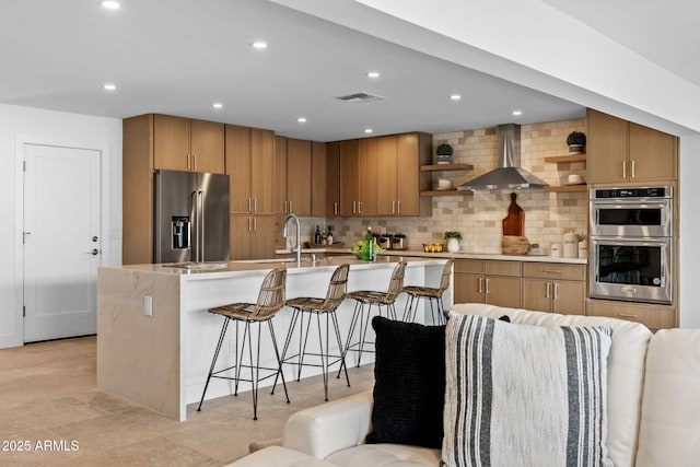 kitchen featuring open shelves, decorative backsplash, wall chimney exhaust hood, a sink, and appliances with stainless steel finishes