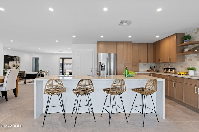 kitchen with open shelves, stainless steel fridge, light countertops, tasteful backsplash, and visible vents