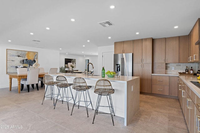 kitchen featuring a sink, a large island, a kitchen bar, visible vents, and high quality fridge