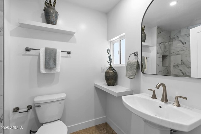 bathroom with a sink, baseboards, walk in shower, and toilet
