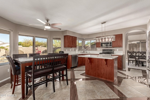 kitchen with stainless steel appliances, ceiling fan, sink, a kitchen island, and hanging light fixtures